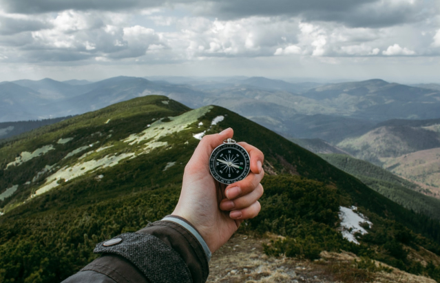 Man holding a compass on a mountain contemplating a professional leadership program