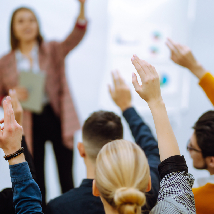 Women leading corporate training programs as people raise hands