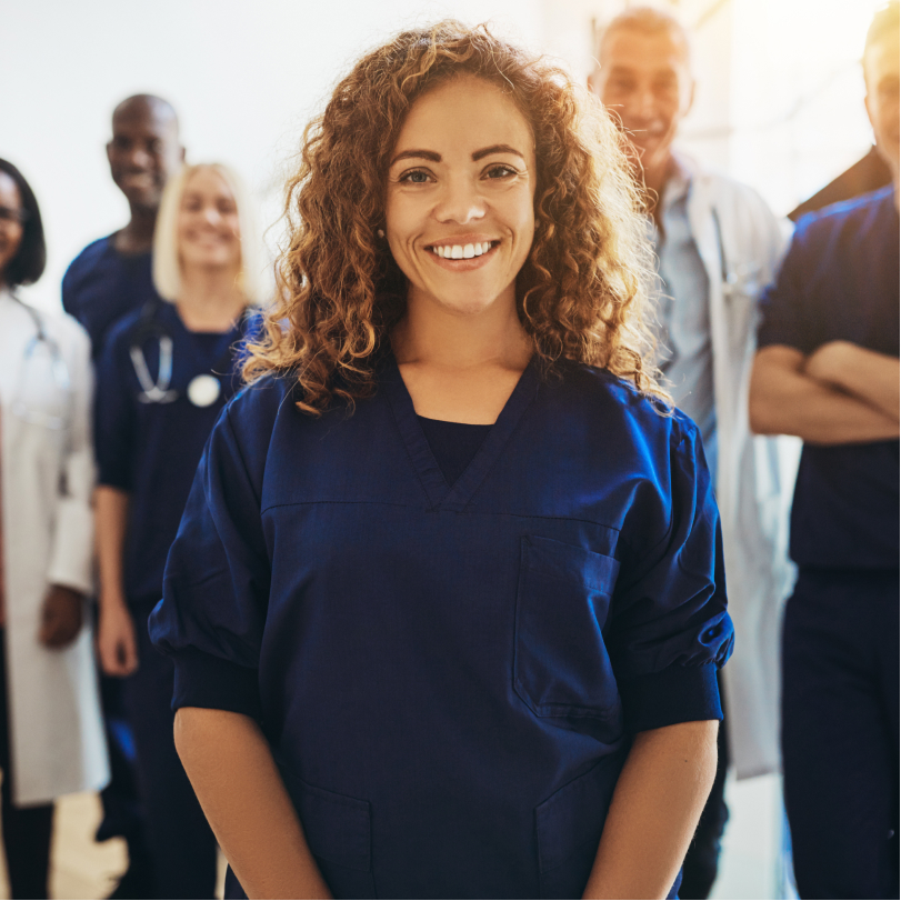 Young nurse with curly hair smiling with coworkers during healthcare leadership training
