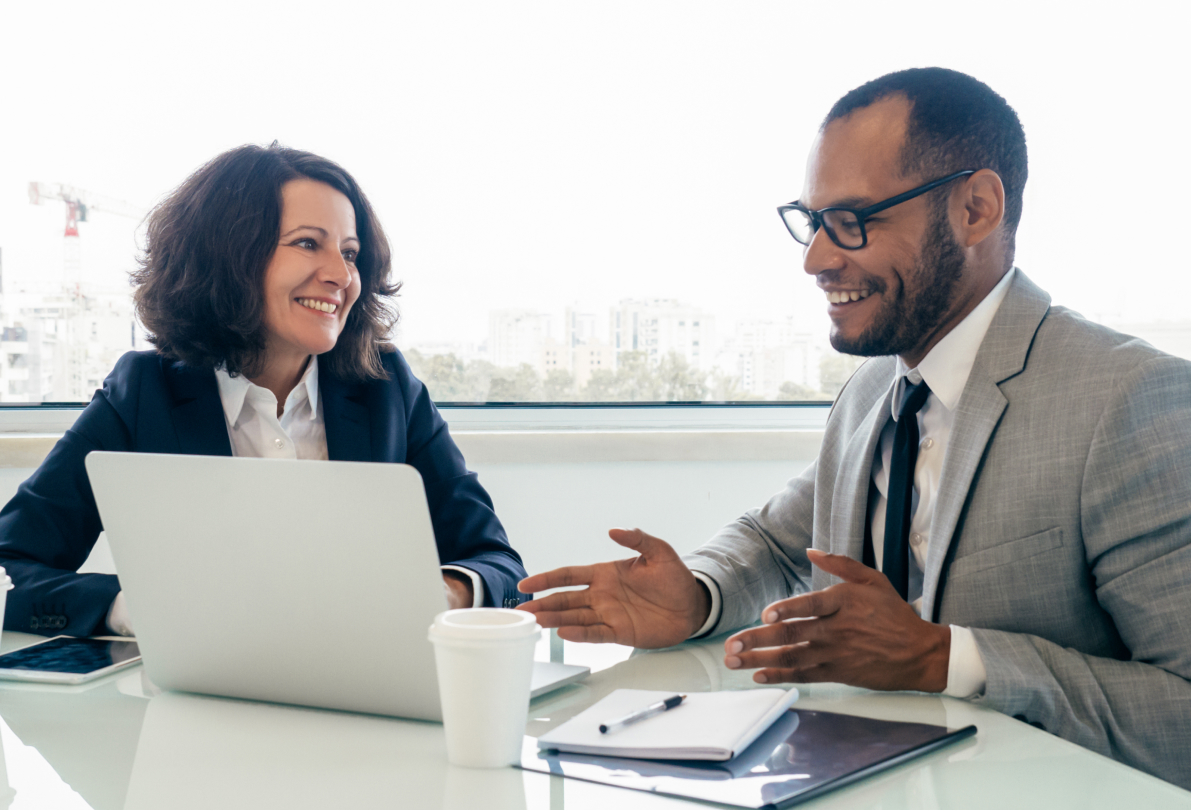Professional man and woman happily discussing corporate training programs by laptop