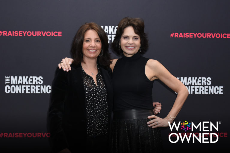 Wendy Leshgold and Lisa McCarthy stand together in front of the Makers Conference backdrop with the Women Owned Business logo in the corner